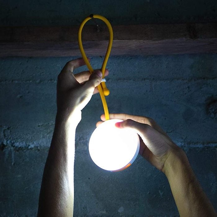 A person holds a glowing round light with a yellow cord, illuminating a dimly lit concrete environment.