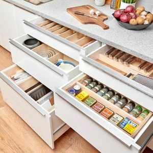Organized kitchen drawers contain utensils, pots, and spices, revealing efficient storage solutions. The countertop displays garlic, vegetables, and a cutting board, enhancing a cooking environment.