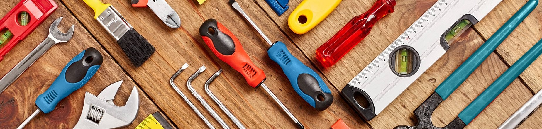Various tools are arranged on a wooden surface, showcasing screwdrivers, wrenches, and a level, indicating preparation for a repair or construction project.