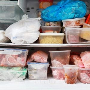Multiple containers filled with frozen food items are haphazardly stacked inside a freezer, creating a cluttered and disorganized appearance.