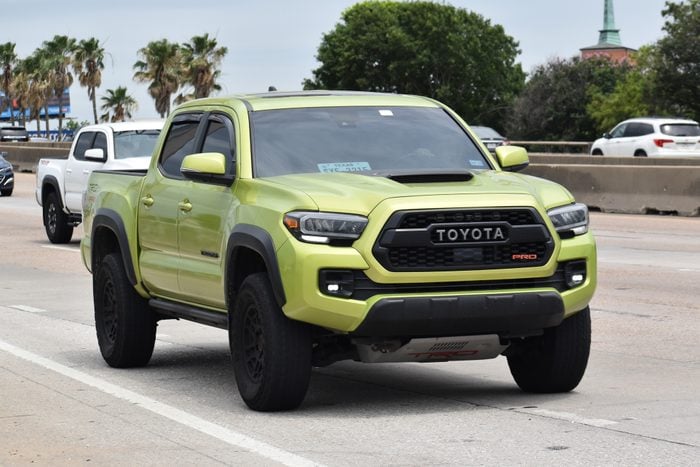 A portrait of a green Toyota Tacoma 4x4 pick-up truck traveling down a highway in moderate traffic
