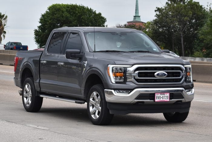 A portrait of a gray Ford F-150 pick-up truck traveling down a highway in moderate traffic