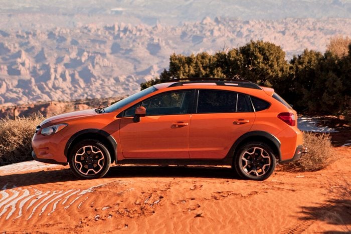 An orange Subaru Crosstrek sits parked on a sand dune with the desert stretching out behind.