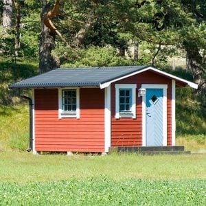 red shed turned into a tiny home in a spacious grassy backyard with a forest behind it