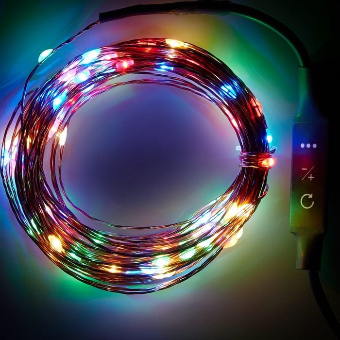 A circular strand of multicolored fairy lights glows brightly, coiled, with a control box attached for adjusting brightness, set against a dark background.